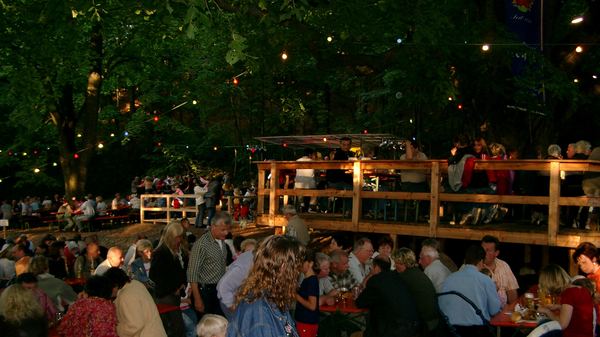 Menschen genießen ein Sommerfest im Freien mit Lichterketten und Holztischen.